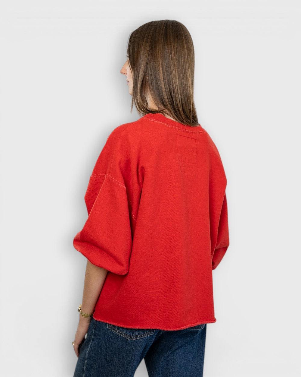 Model wearing a red JONES + CO Fond sweatshirt with drop shoulders, cropped sleeves, and a raw edge hemline.