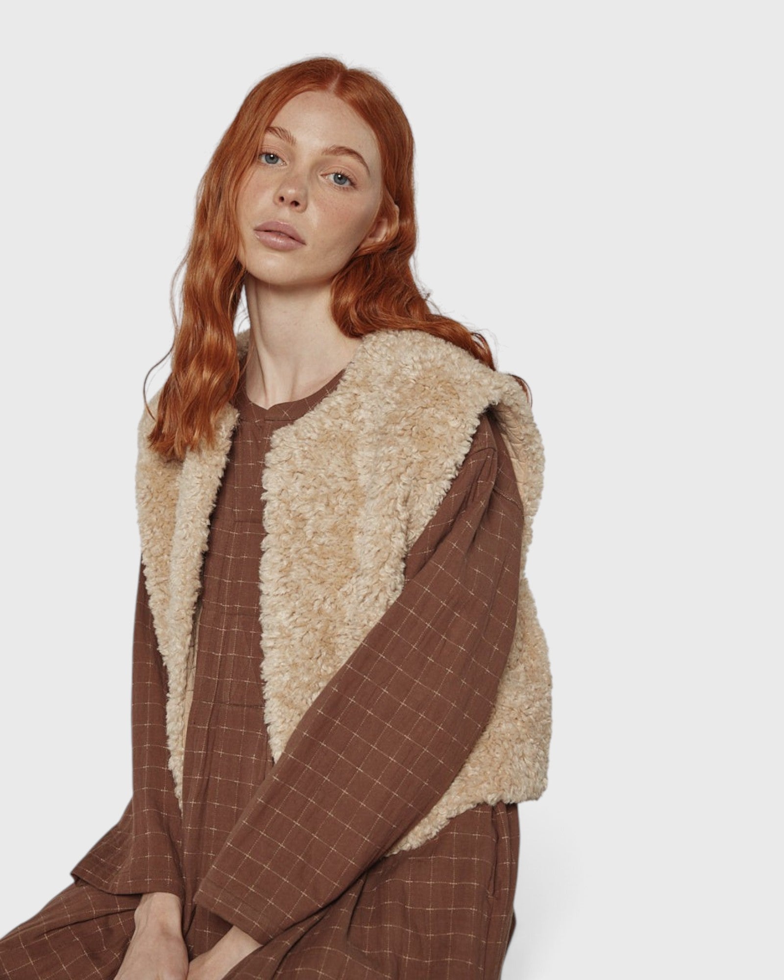 JONES + CO reversible short vest in oatmeal faux fur worn over a brown plaid dress by a red-haired model