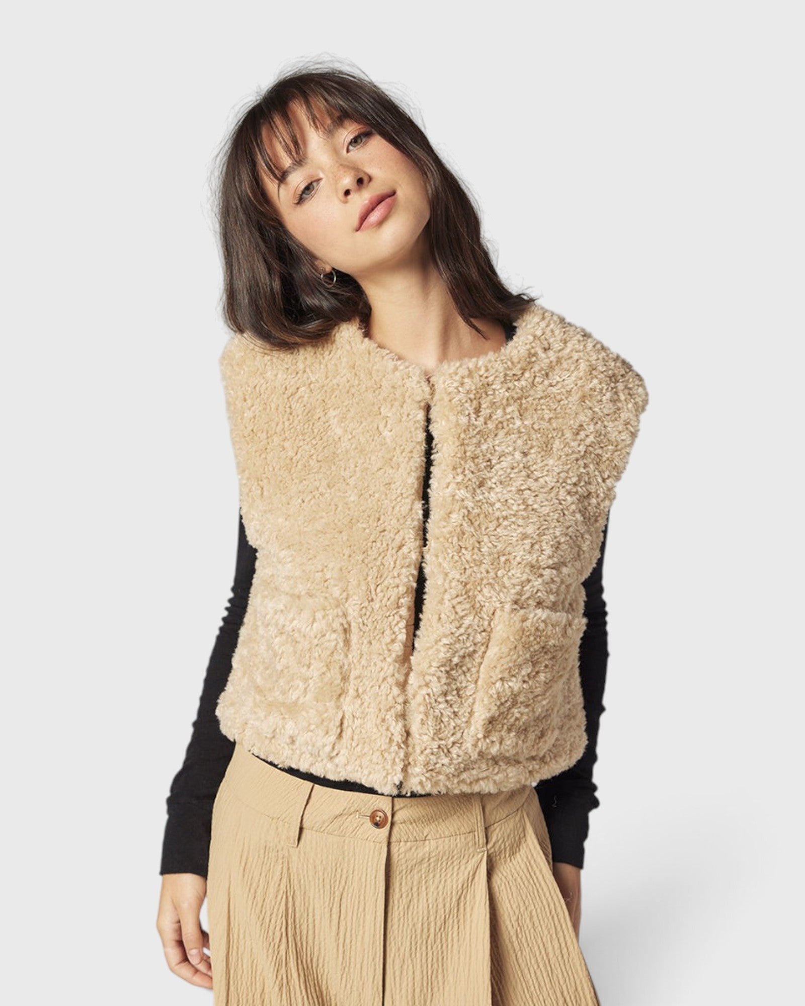 JONES + CO reversible short vest in oatmeal faux fur worn by a model over a black long-sleeve top