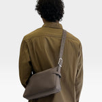 JONES + CO Rider S taupe calf leather crossbody bag with adjustable belt-style strap worn by a man in a brown shirt