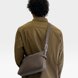 JONES + CO Rider S taupe calf leather crossbody bag with adjustable belt-style strap worn by a man in a brown shirt