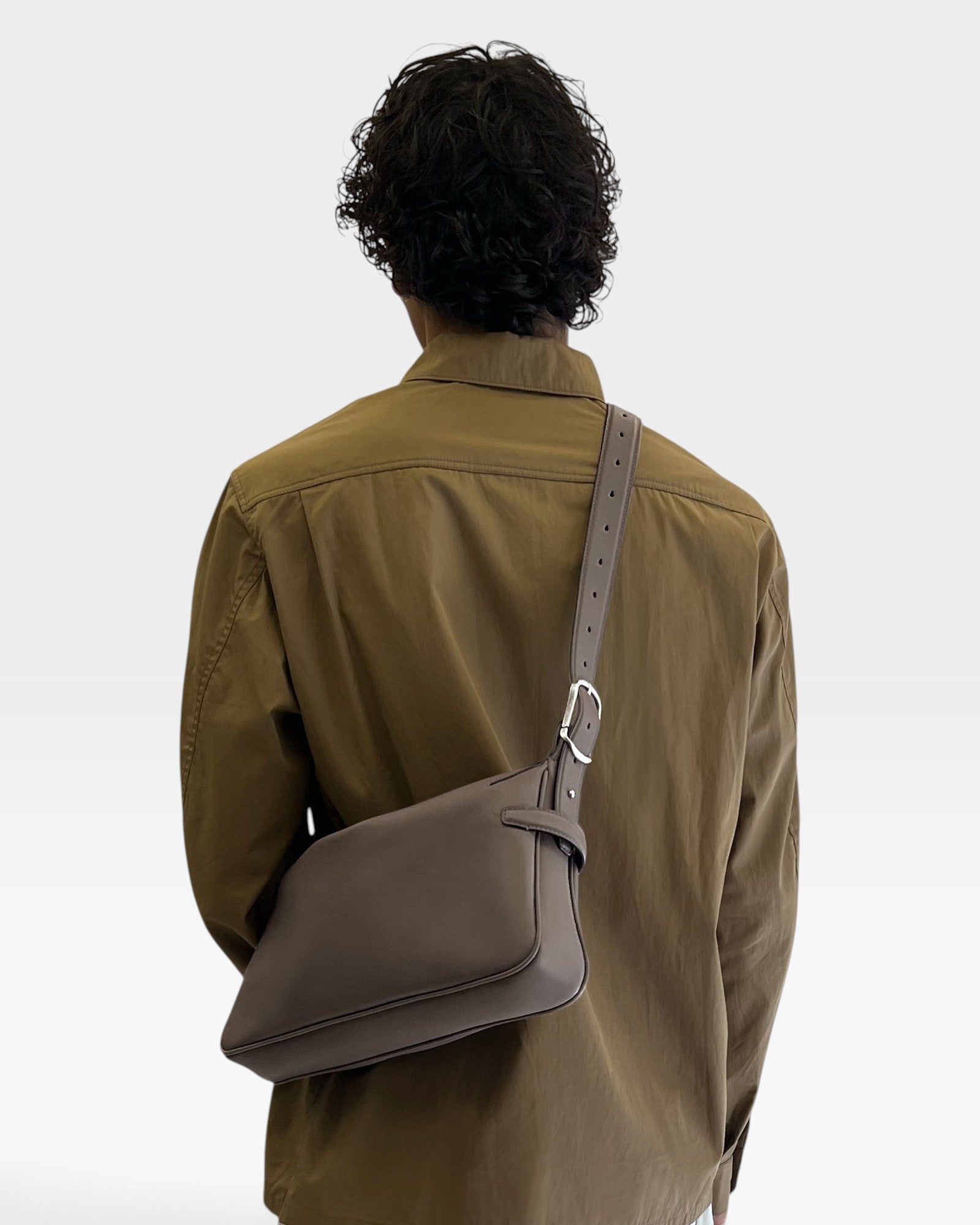 JONES + CO Rider S taupe calf leather crossbody bag with adjustable belt-style strap worn by a man in a brown shirt