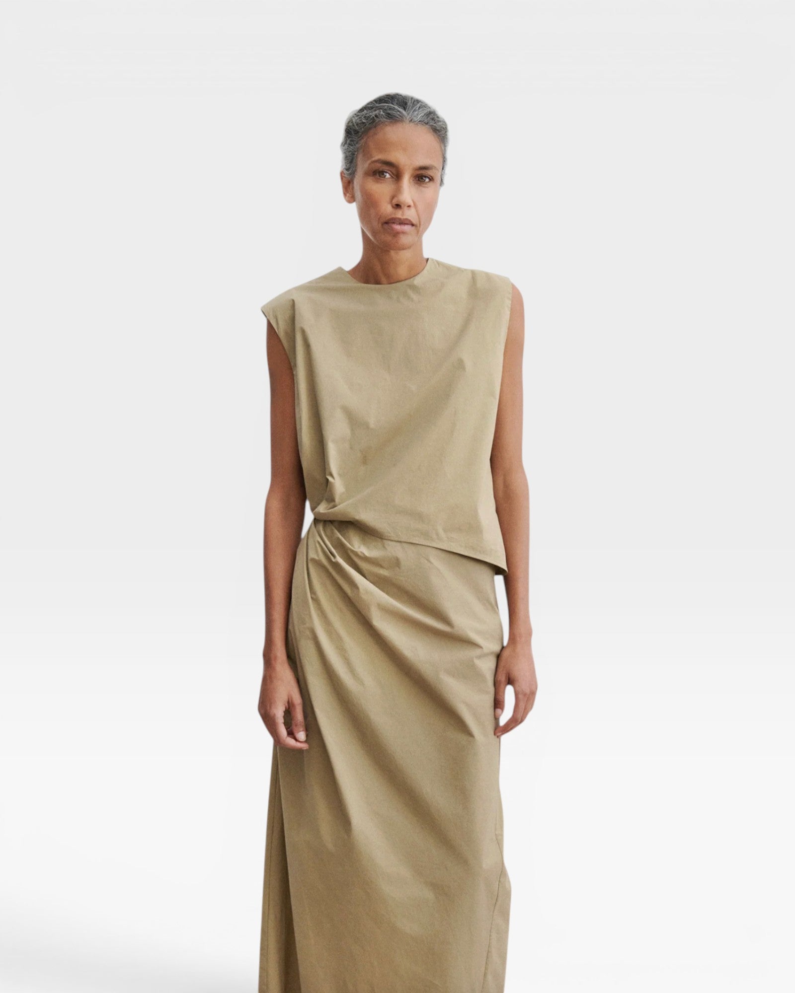 JONES + CO Rini Dress in khaki cotton features an asymmetrical sleeveless top and a draped straight skirt with a side pleat.