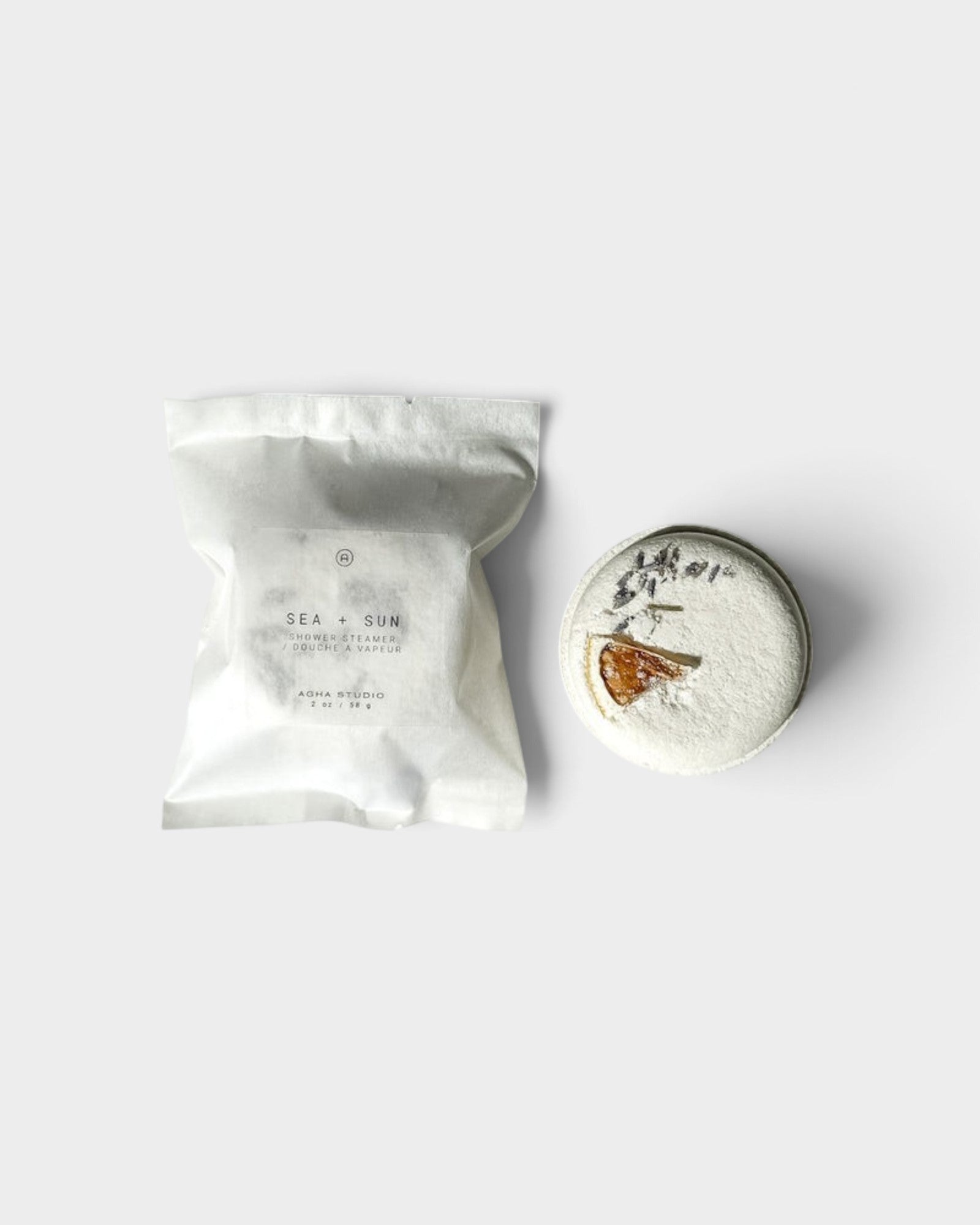 JONES + CO Sea + Sun shower steamer in white packaging next to a round, citrus-topped aromatherapy shower tablet.