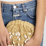 JONES + CO natural raffia crochet clutch adorned with shell and bead embellishments, worn with blue jeans.