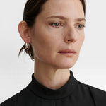 JONES + CO silver-plated brass chunky tapered huggie hoop earrings worn by a model in a black top