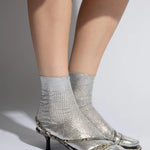 JONES + CO silver laminated ribbed silk socks with metallic foil overlay, worn with open-toe heels.