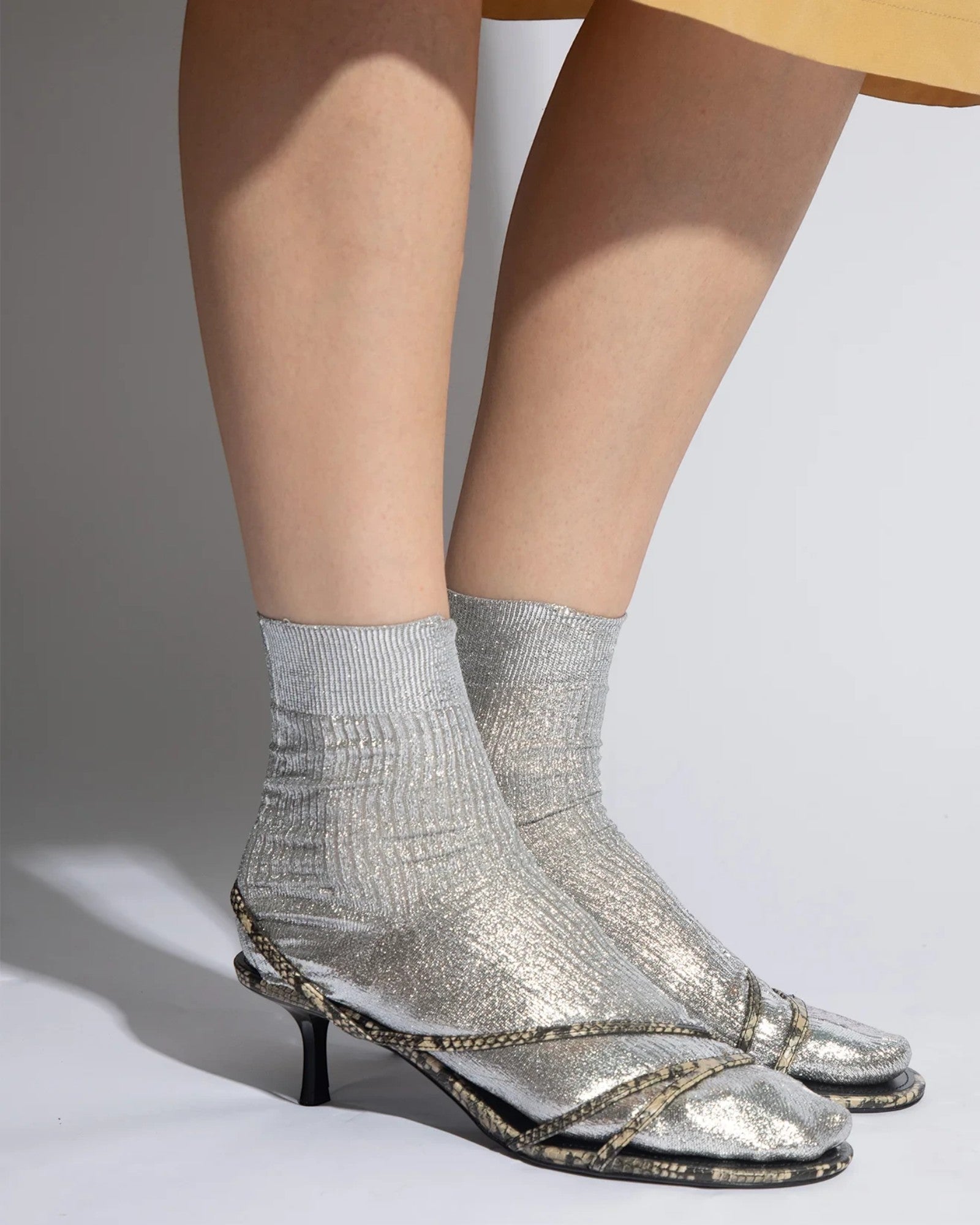 JONES + CO silver laminated ribbed silk socks with metallic foil overlay, worn with open-toe heels.