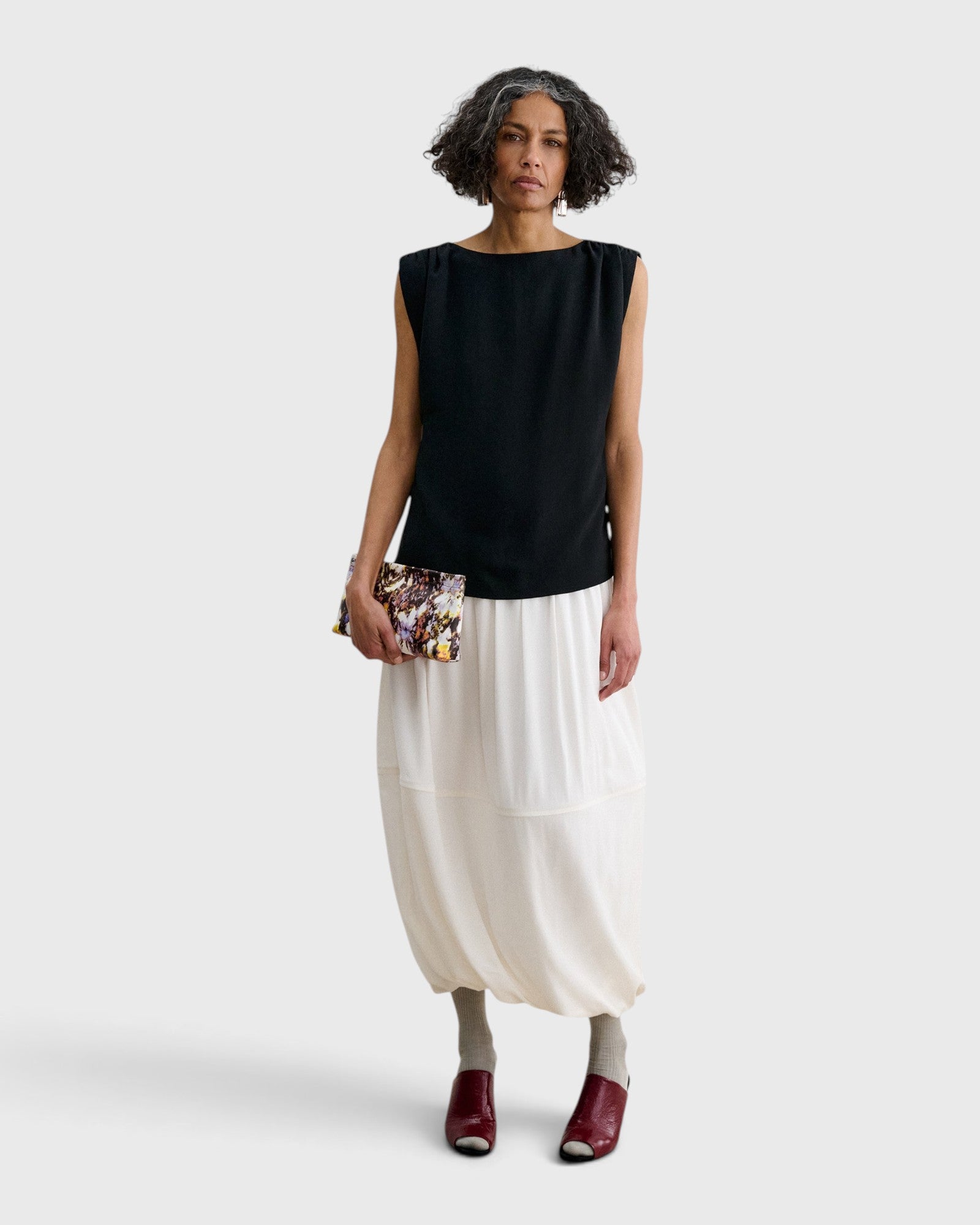 Model holding a JONES + CO Small Hinge Clutch with a colorful abstract floral watercolor print and structured design.