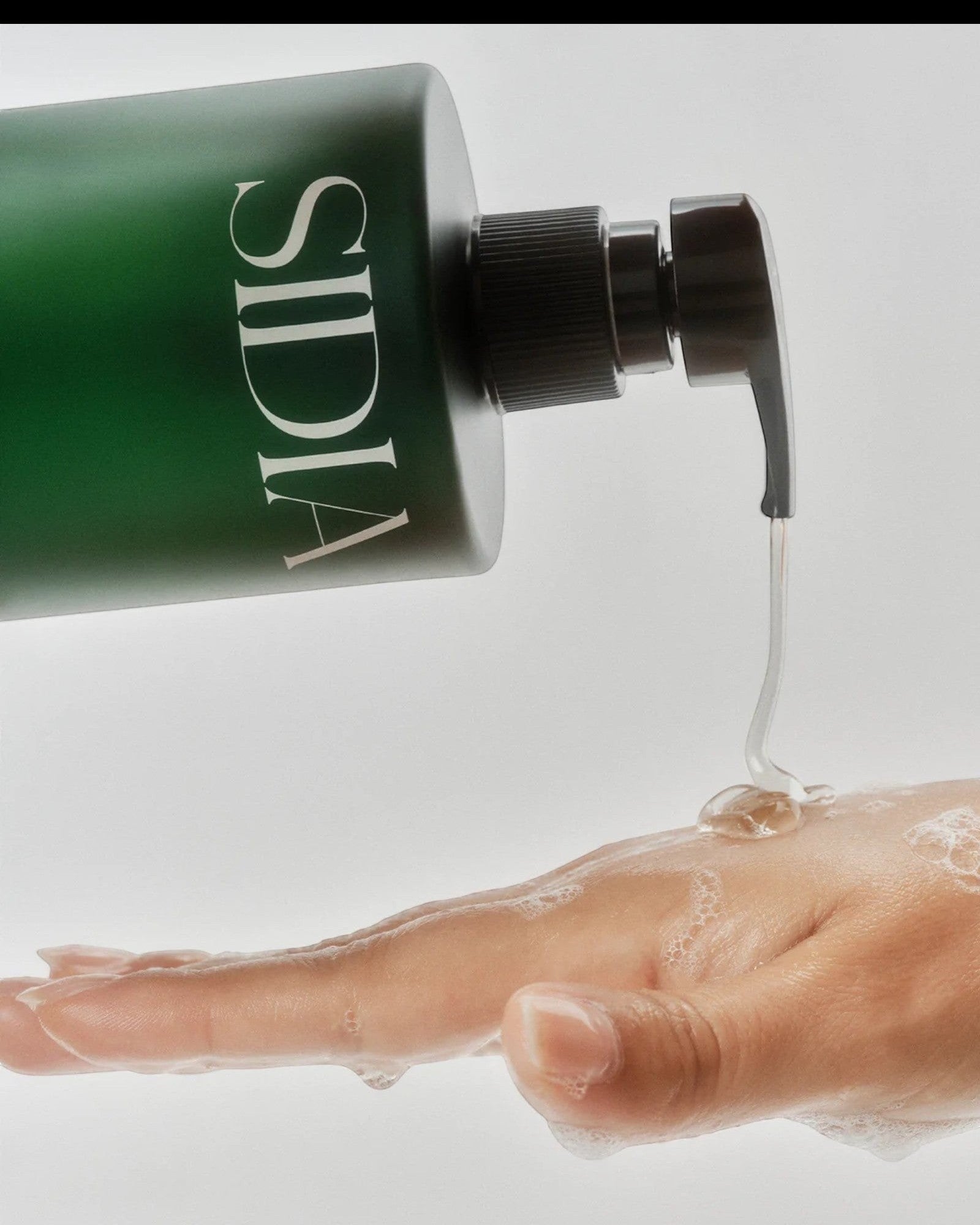 JONES + CO The SOAKED Wash, a champagne-hued hand and body cleanser with avocado butter and shea butter, being dispensed onto a soapy hand.