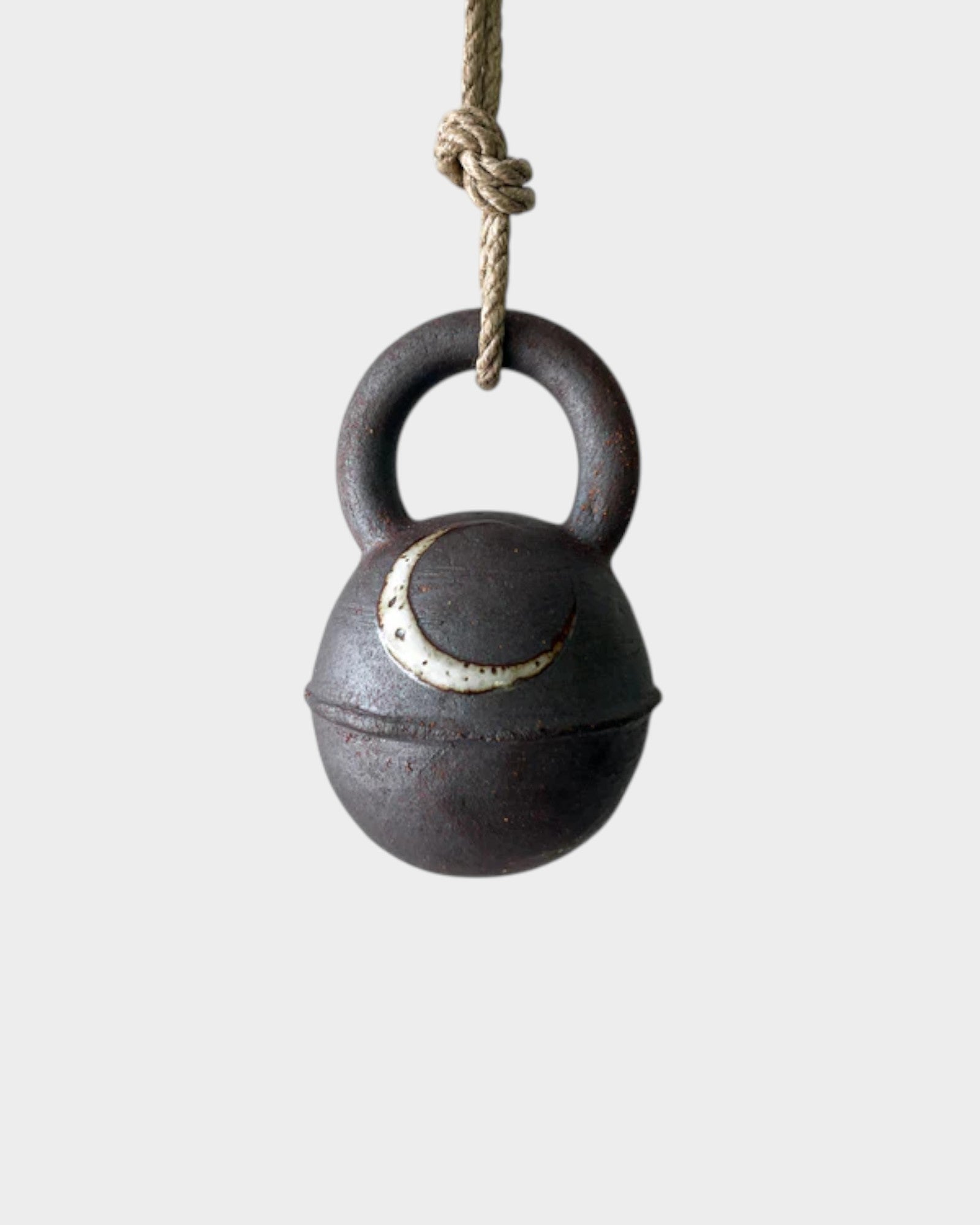 JONES + CO round extra dark stoneware jingle bell featuring a hand-painted crescent moon, hanging on a hemp rope.