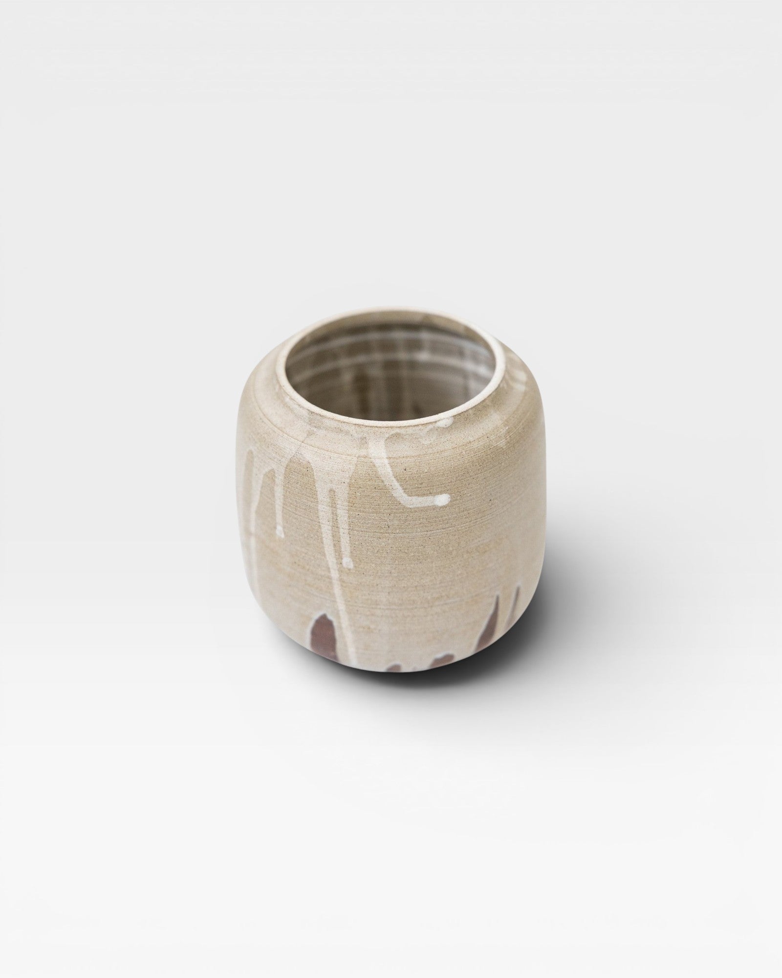 JONES + CO handcrafted stoneware pot with smooth cylindrical shape, beige finish, and white glaze drips. Modern artisan style.