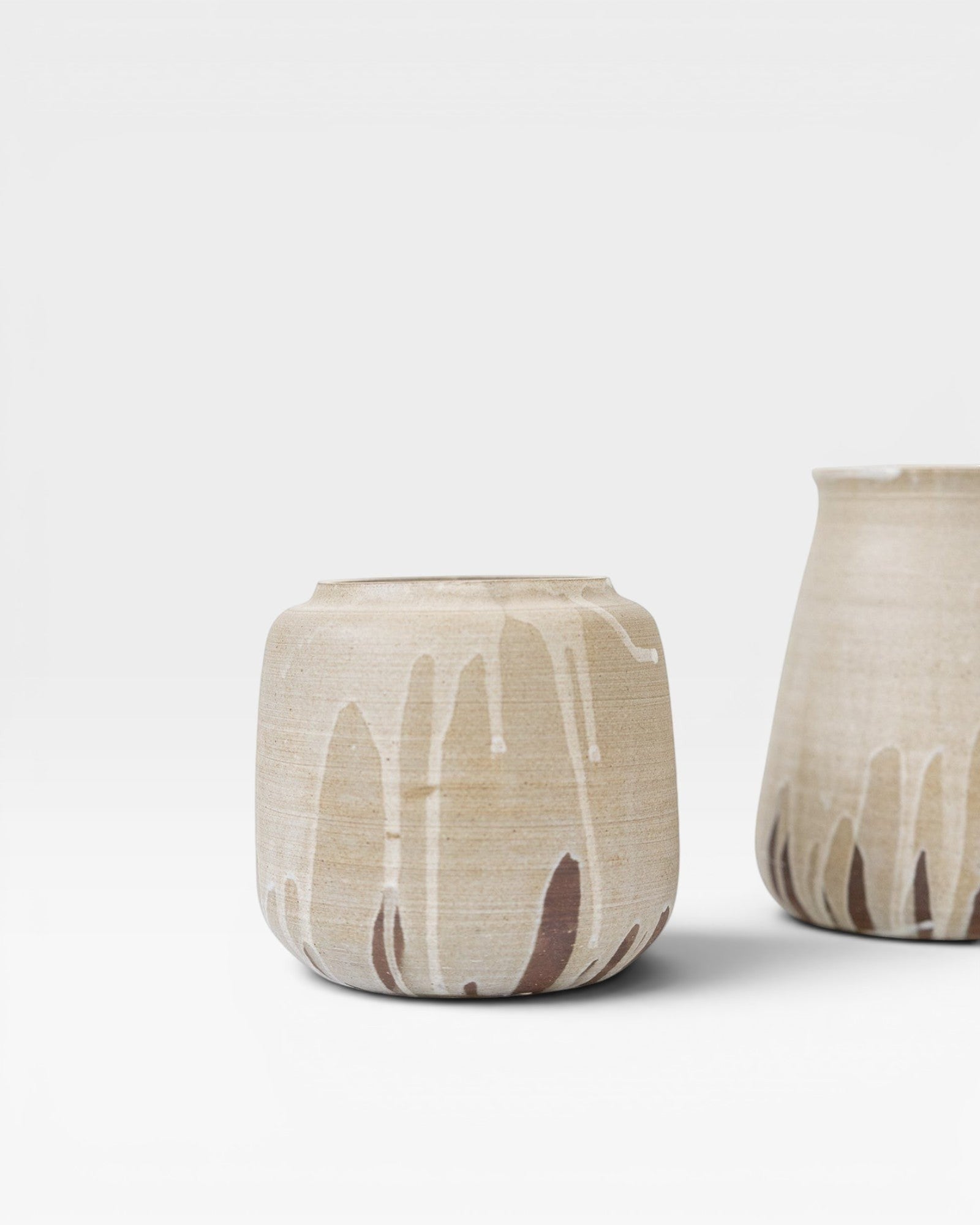 JONES + CO handcrafted stoneware pot with beige finish and white glaze drips. Cylindrical shape, modern artisan style.
