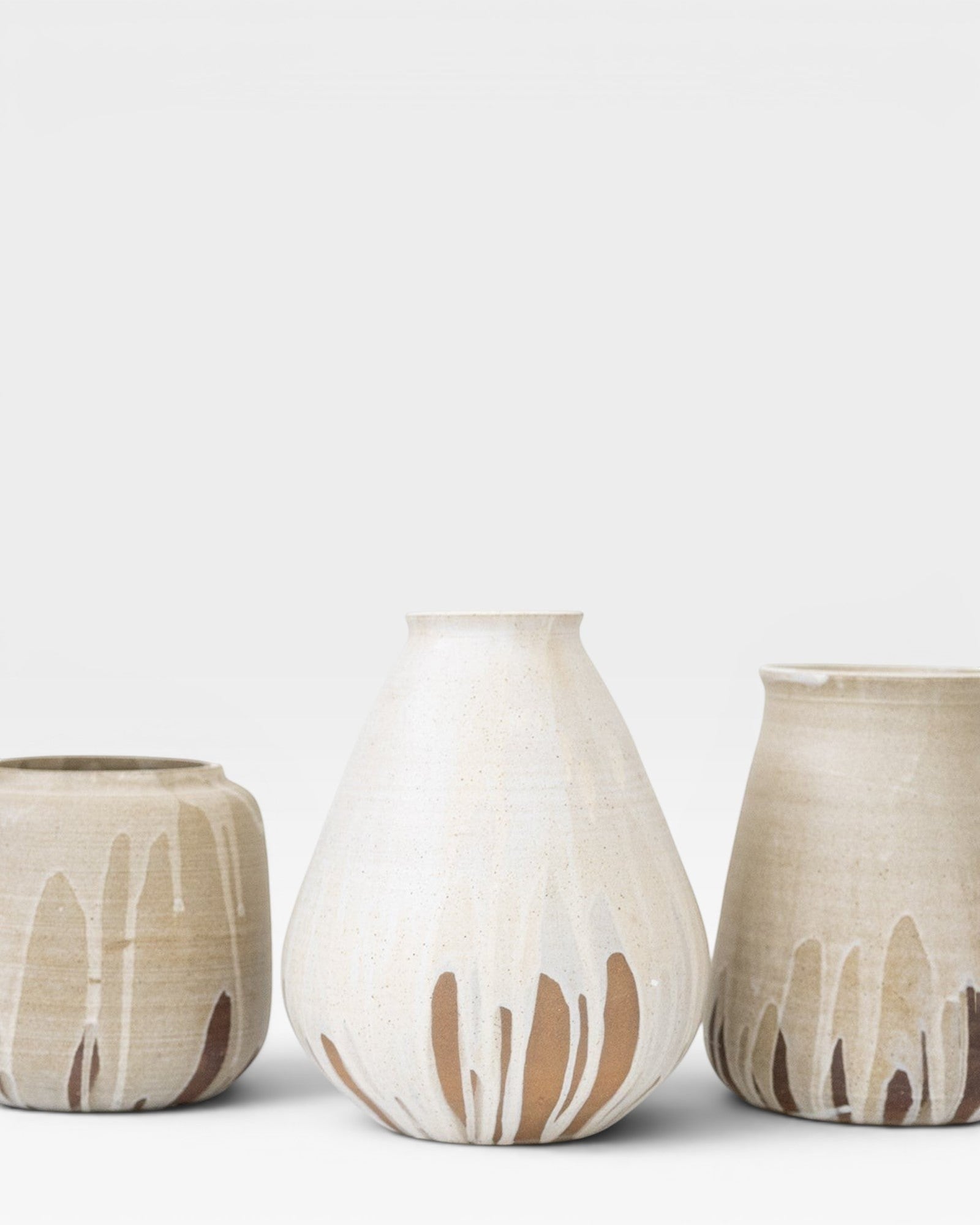 JONES + CO handcrafted beige stoneware pot with white glaze drips and smooth cylindrical shape.