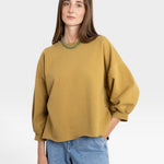 JONES + CO mustard yellow crewneck sweatshirt with drop shoulders, raw hem, and cropped sleeves. Model wears light wash jeans.
