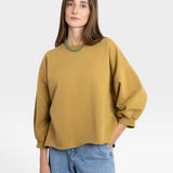 JONES + CO mustard yellow crewneck sweatshirt with drop shoulders, raw hem, and cropped sleeves. Model wears light wash jeans.