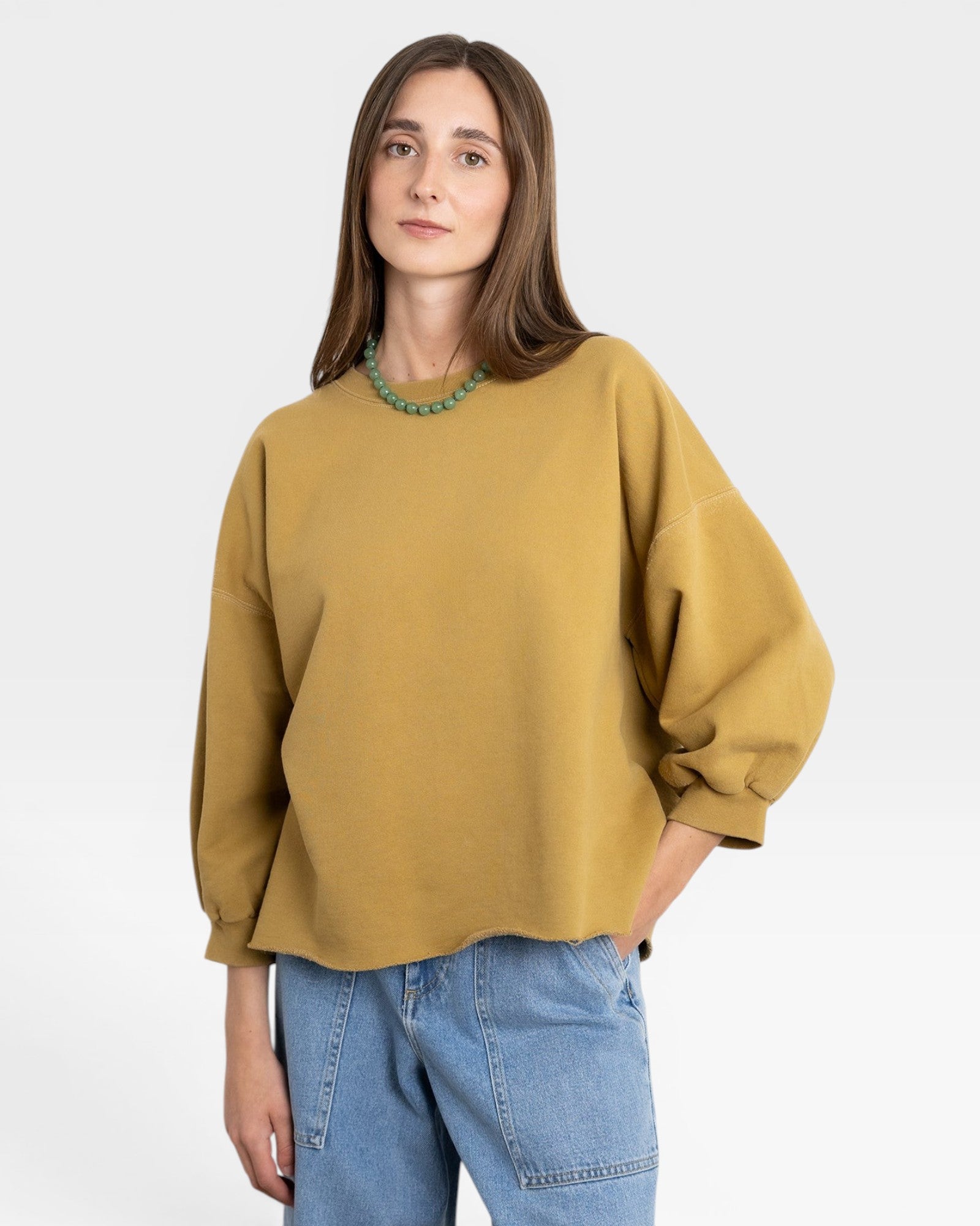 JONES + CO mustard yellow crewneck sweatshirt with drop shoulders, raw hem, and cropped sleeves. Model wears light wash jeans.