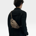 JONES + CO Bon-Bon taupe leather shoulder bag with pleated ends and silver hardware worn by a model in a black coat
