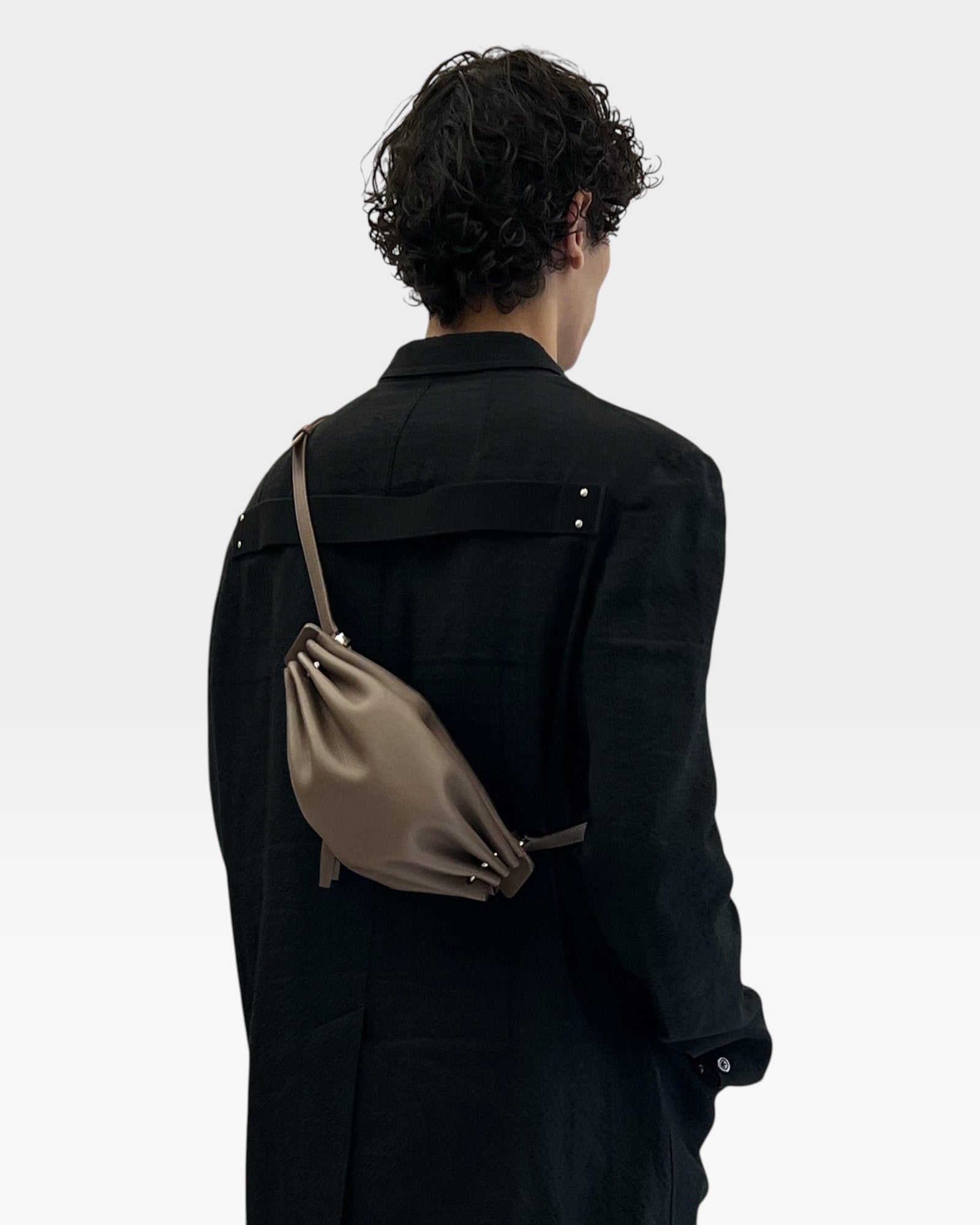 JONES + CO Bon-Bon taupe leather shoulder bag with pleated ends and silver hardware worn by a model in a black coat
