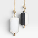 JONES + CO Thrown Bell - Domino Indigo, two ceramic bells hanging from rope. One bell is white with a large white oval detail. The other is half black, half white.