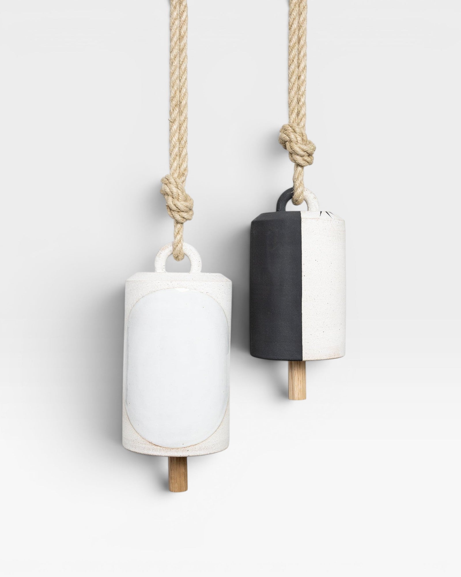 JONES + CO Thrown Bell - Domino Indigo, two ceramic bells hanging from rope. One bell is white with a large white oval detail. The other is half black, half white.