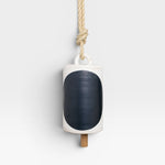 JONES + CO Thrown Bell in Domino Indigo, a white ceramic bell with a large indigo oval and a wooden clapper, hung by a rope.