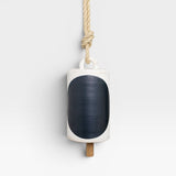 JONES + CO Thrown Bell in Domino Indigo, a white ceramic bell with a large indigo oval and a wooden clapper, hung by a rope.