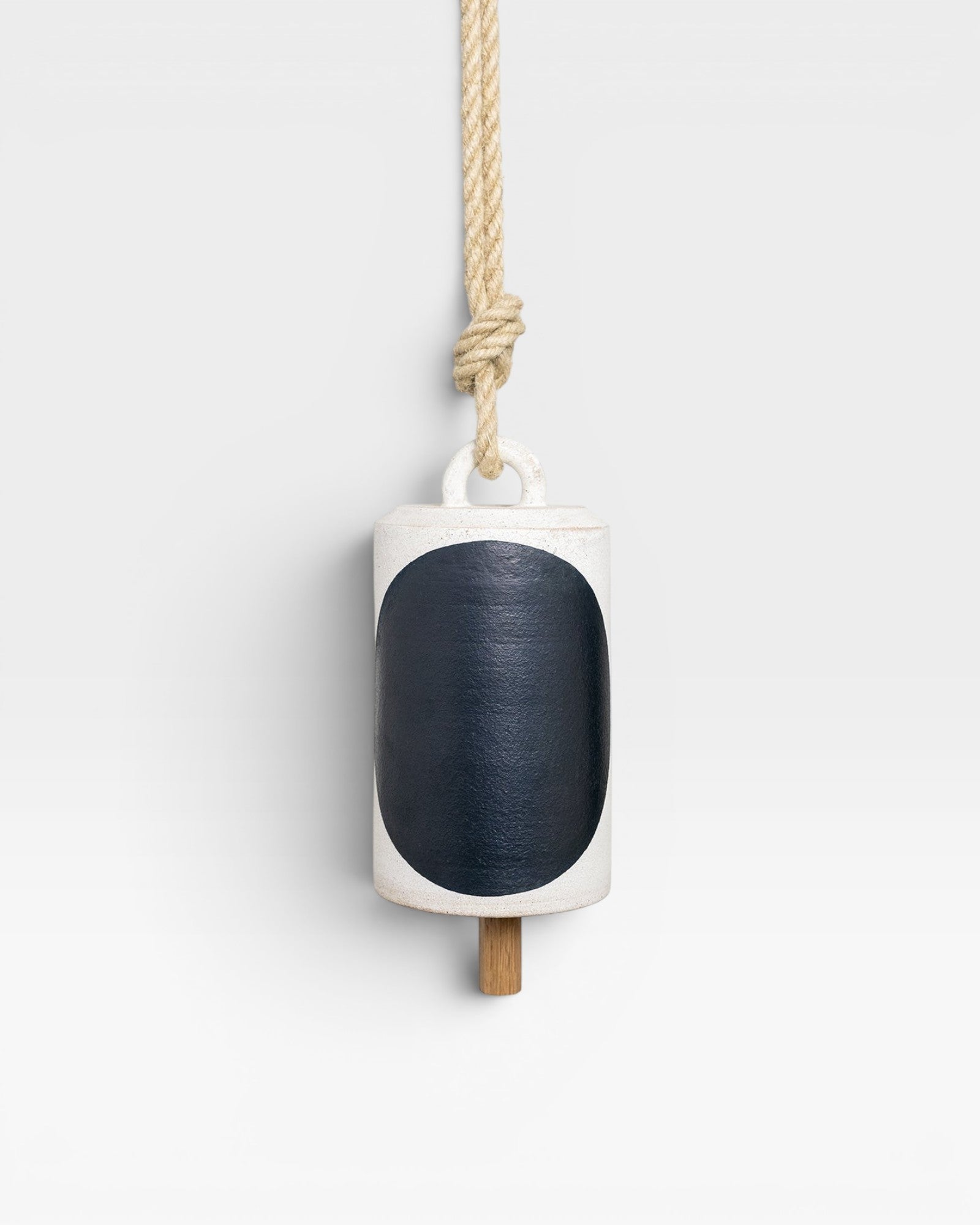 JONES + CO Thrown Bell in Domino Indigo, a white ceramic bell with a large indigo oval and a wooden clapper, hung by a rope.