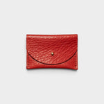 JONES + CO tomato red leather cardholder with a solid brass fastener, front view on a light grey background.