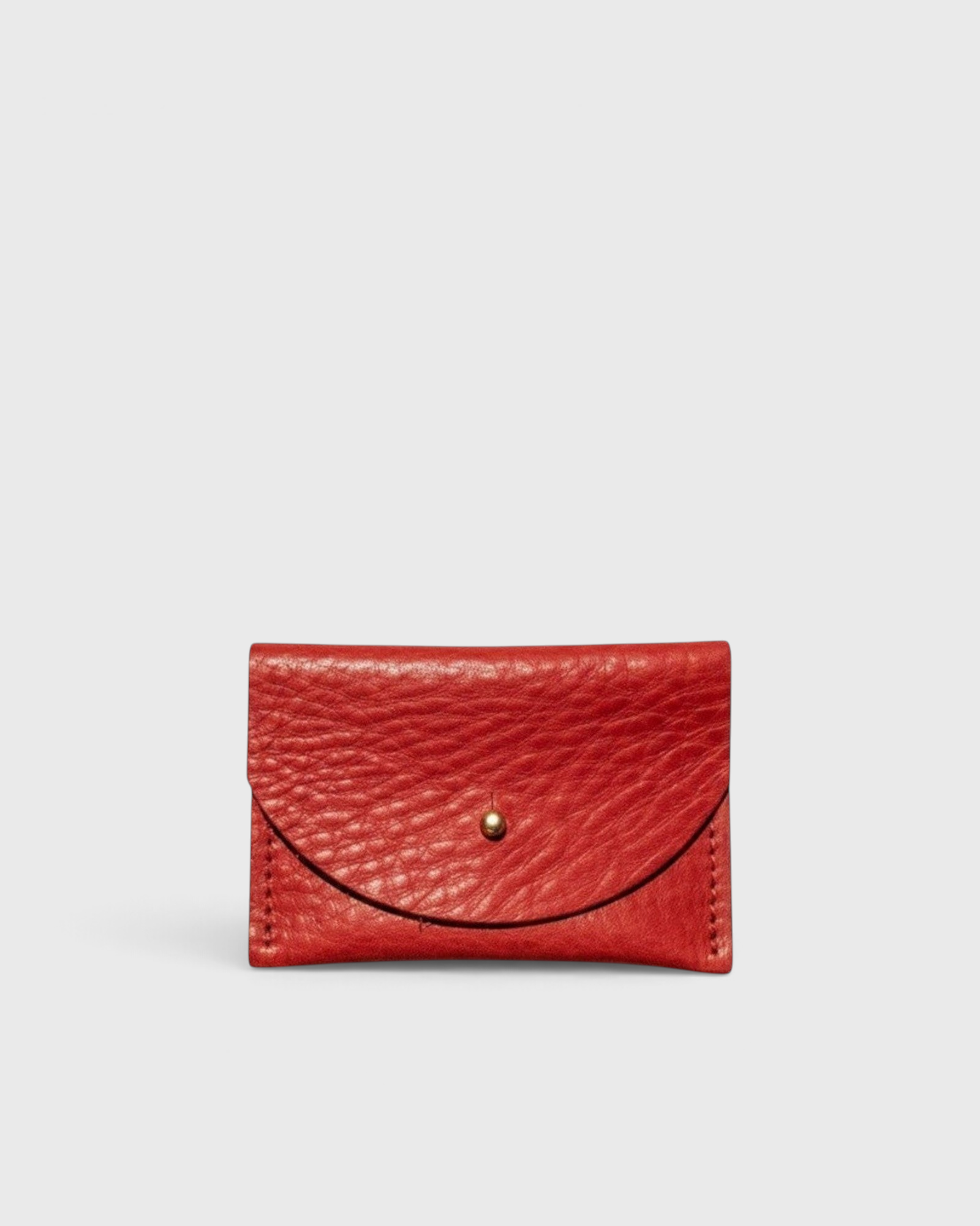 JONES + CO tomato red leather cardholder with a solid brass fastener, front view on a light grey background.