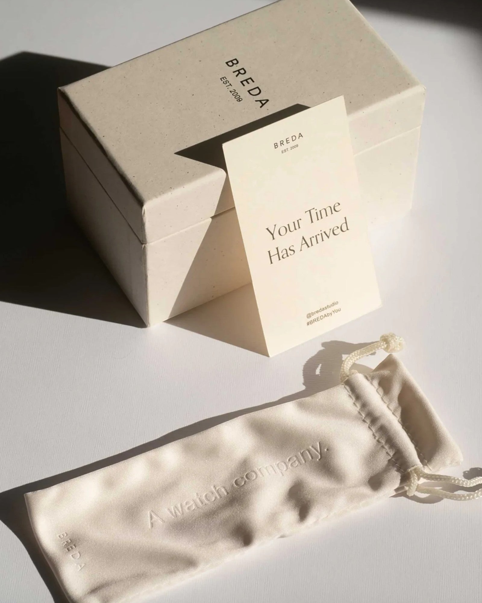 JONES + CO branded watch packaging including a beige gift box, a greeting card, and a soft drawstring pouch.