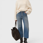 Model wearing JONES + CO Wera mid blue wide-leg cropped denim jeans with a cream cable knit sweater and dark tote bag