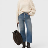 Model wearing JONES + CO Wera mid blue wide-leg cropped denim jeans with a cream cable knit sweater and dark tote bag