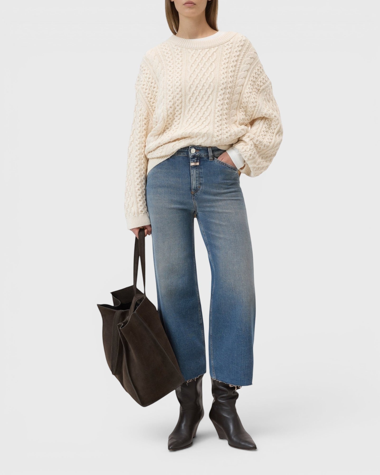 Model wearing JONES + CO Wera mid blue wide-leg cropped denim jeans with a cream cable knit sweater and dark tote bag