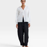 JONES + CO white organic cotton voile blouse with voluminous sleeves, gathered cuffs, deep V-neck, and mother-of-pearl buttons. Subtle checkered pattern.