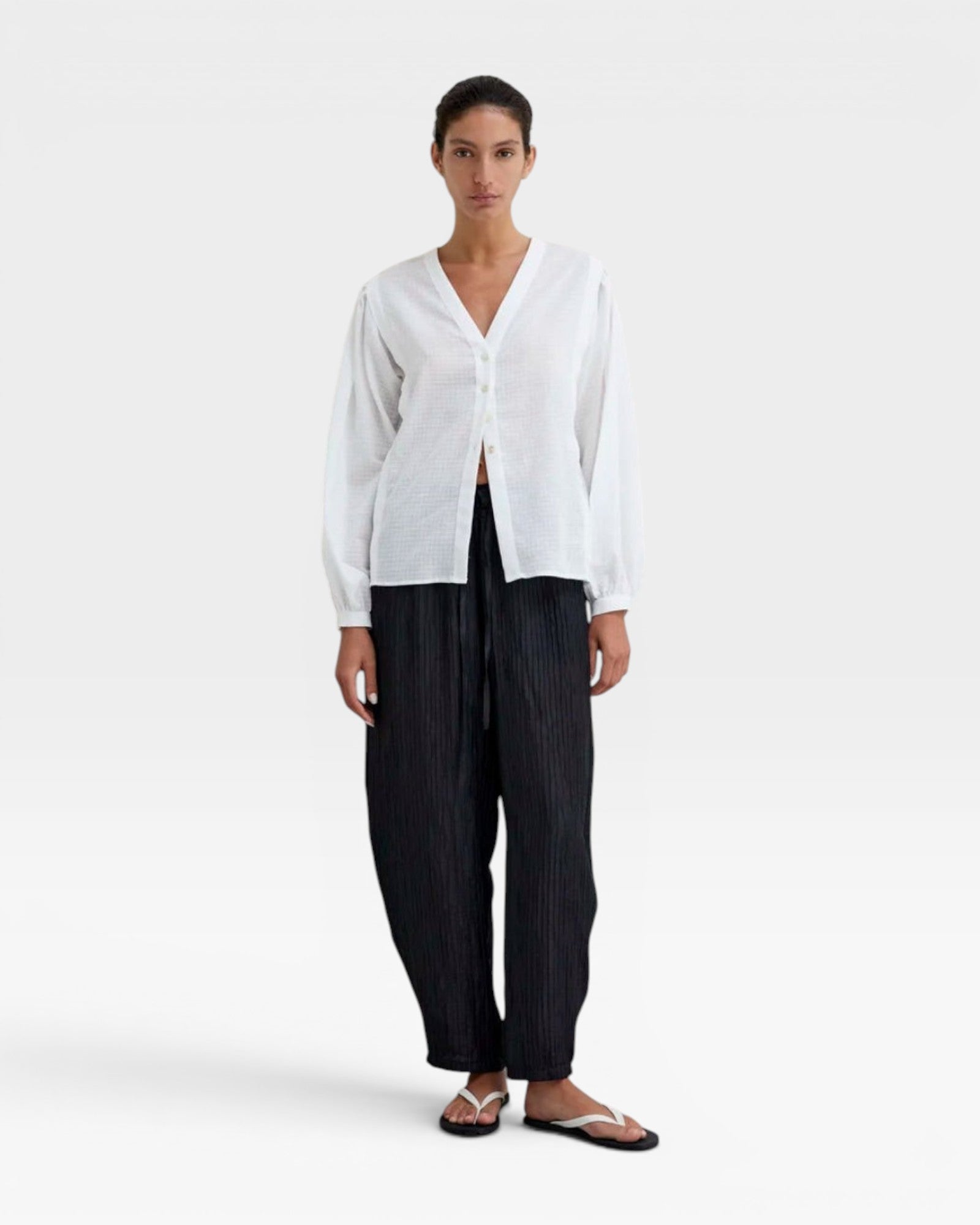 JONES + CO white organic cotton voile blouse with voluminous sleeves, gathered cuffs, deep V-neck, and mother-of-pearl buttons. Subtle checkered pattern.