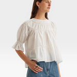 JONES + CO white 100% Pima cotton lawn Sol top with boat neck, crochet trim, puff sleeves, and ruffle cuffs.