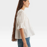 JONES + CO white 100% Pima cotton lawn Sol top with boat neck, crochet trim, puff sleeves, and ruffle cuffs.