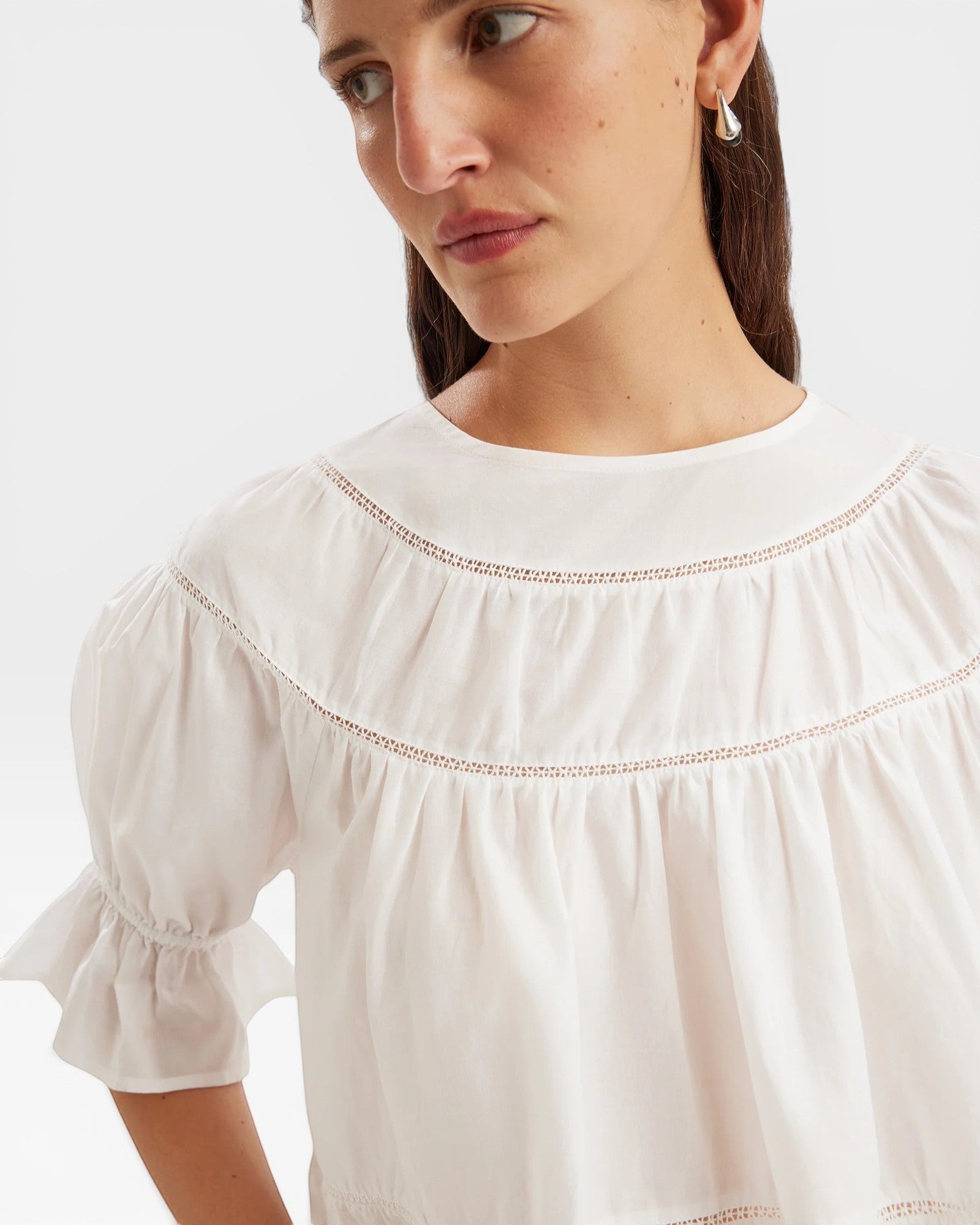 JONES + CO white 100% Pima cotton lawn Sol top with crochet lace trim, boat neck, puff sleeves, and ruffle cuffs.