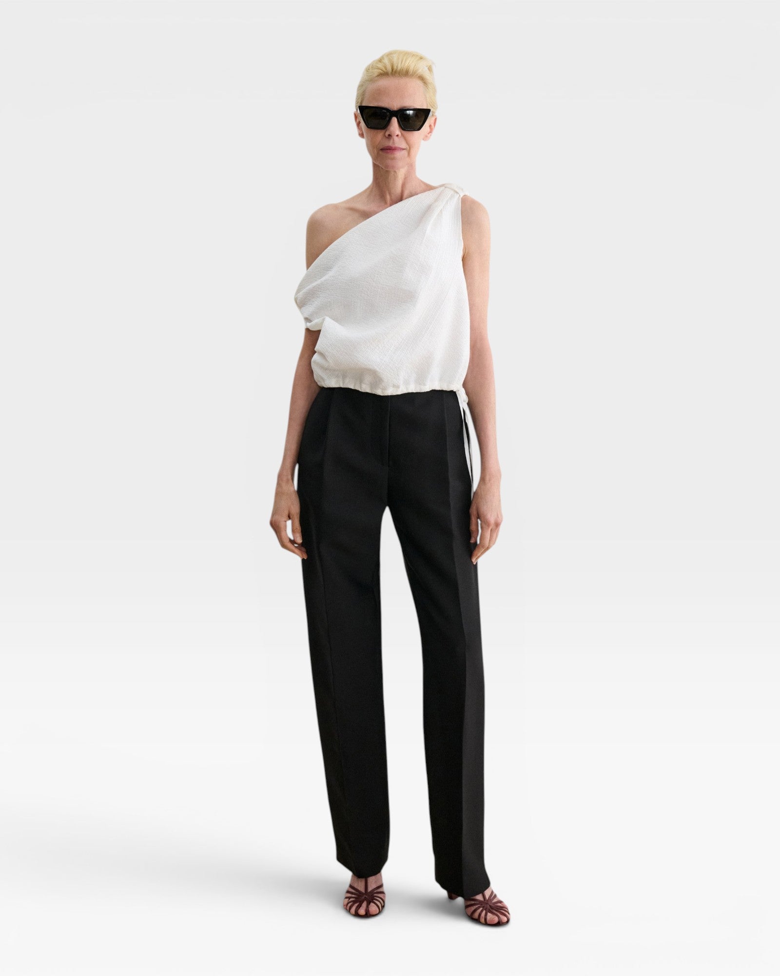 Model wearing JONES + CO white one-shoulder Farfalla top in Italian Foam fabric with draped silhouette and drawstring.