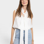 JONES + CO white sleeveless blouse with tie-neck detail, paired with light wash jeans. Model is wearing a gold bracelet.