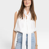 JONES + CO white sleeveless blouse with tie-neck detail, paired with light wash jeans. Model is wearing a gold bracelet.