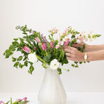 JONES + CO white speckled ceramic bulb vase with a bouquet of pink and white flowers.