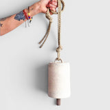 JONES + CO white stoneware bell with a star detail, beveled wood knocker, and hemp rope held by a tattooed hand.