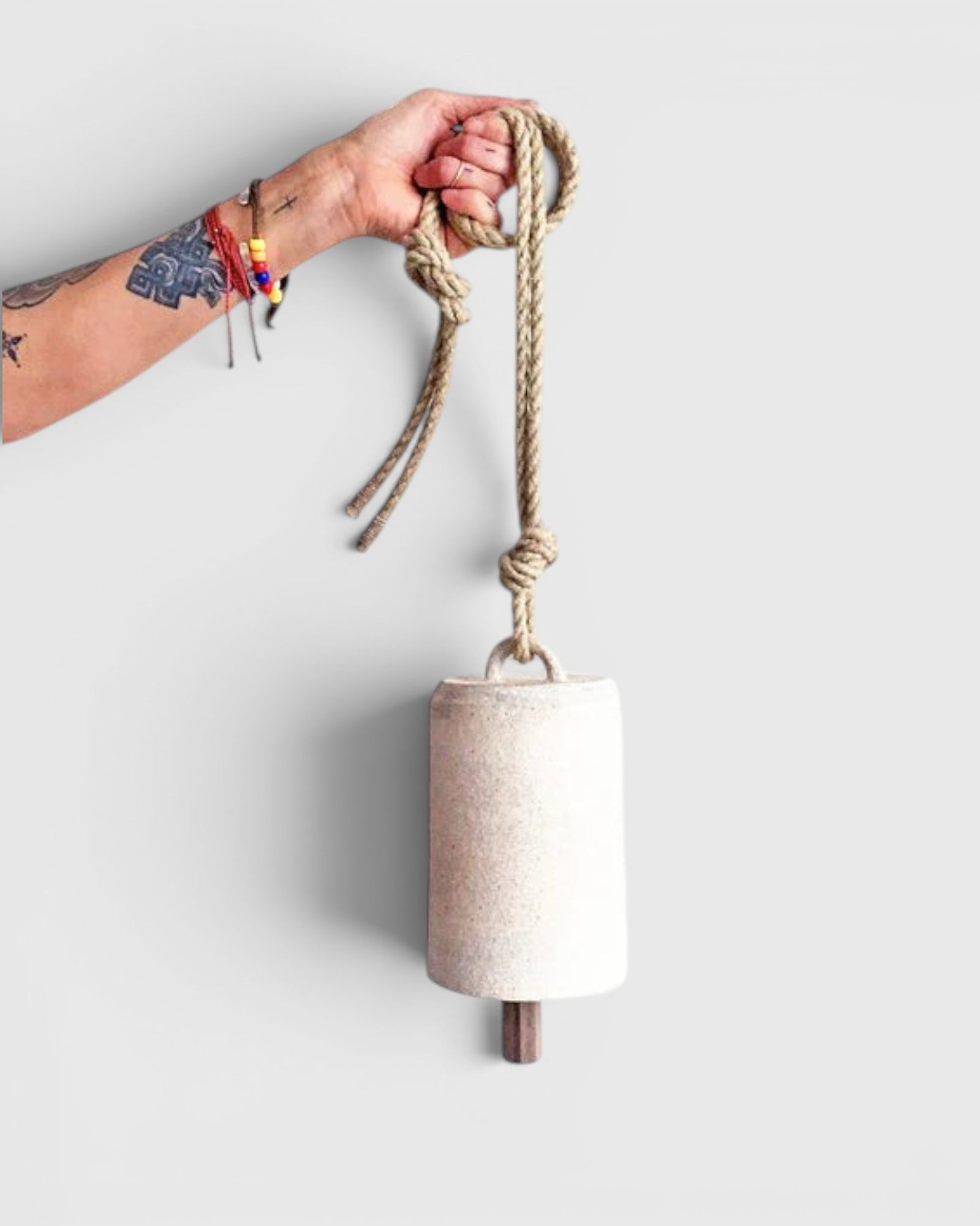 JONES + CO white stoneware bell with a star detail, beveled wood knocker, and hemp rope held by a tattooed hand.