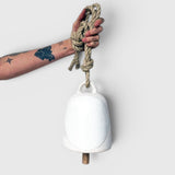 JONES + CO round stoneware bell in full moon white with a wooden knocker and hemp rope held by a tattooed hand