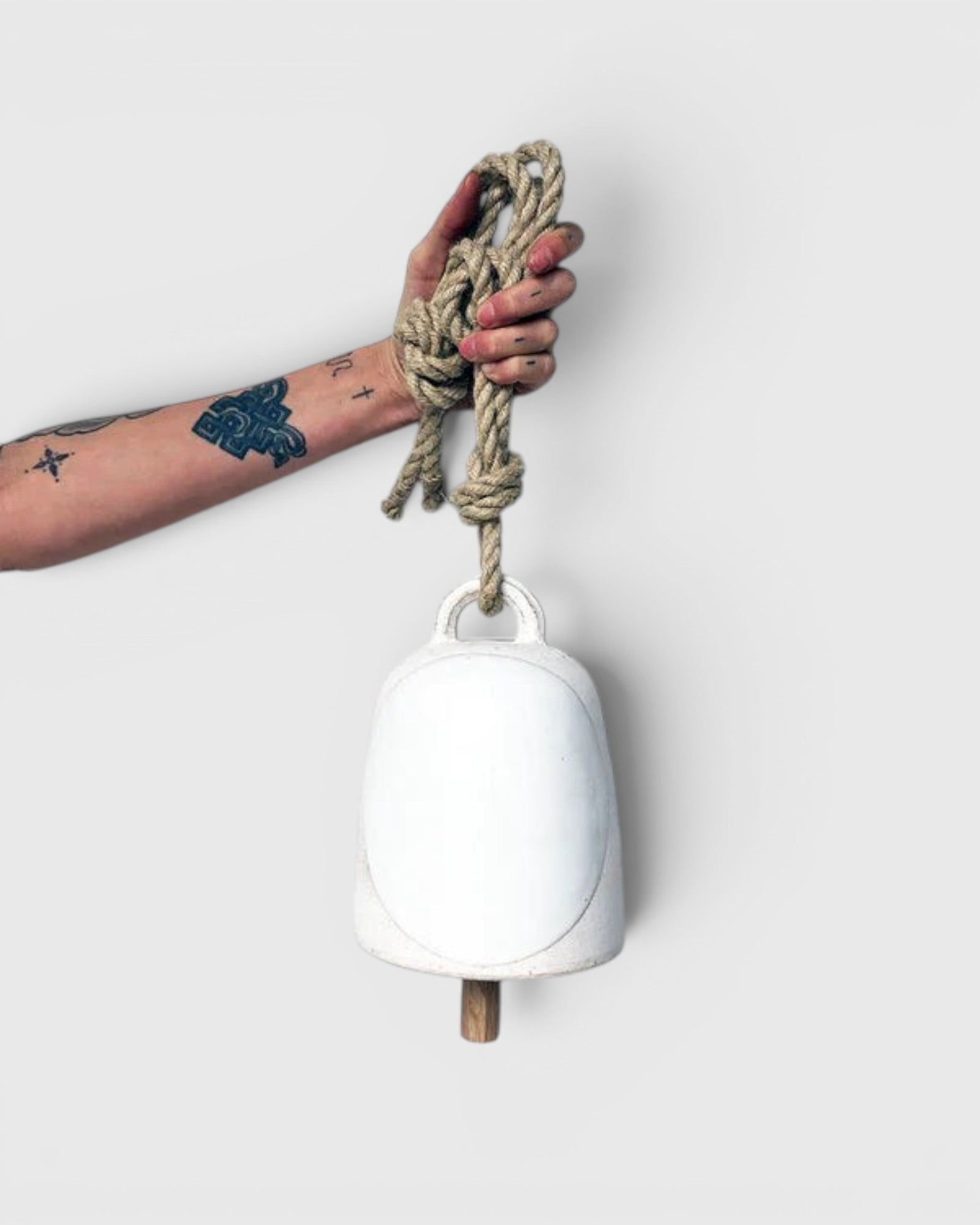 JONES + CO round stoneware bell in full moon white with a wooden knocker and hemp rope held by a tattooed hand