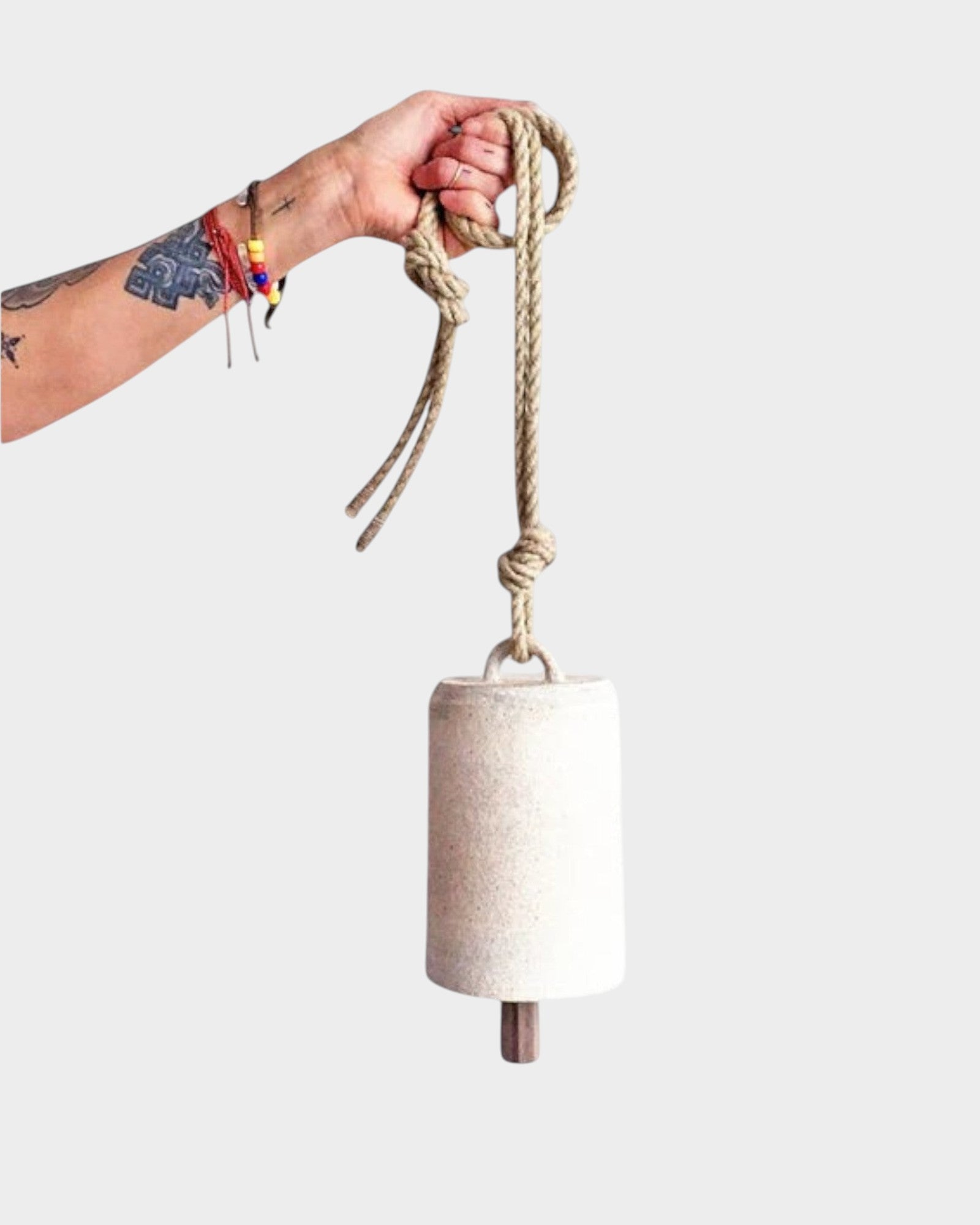 JONES + CO white stoneware bell with a star detail, beveled wood knocker, and hemp rope held by a tattooed hand.