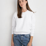Model wearing a JONES + CO white Ziggy sweatshirt with a crew neck and cropped sleeves, paired with blue jeans.