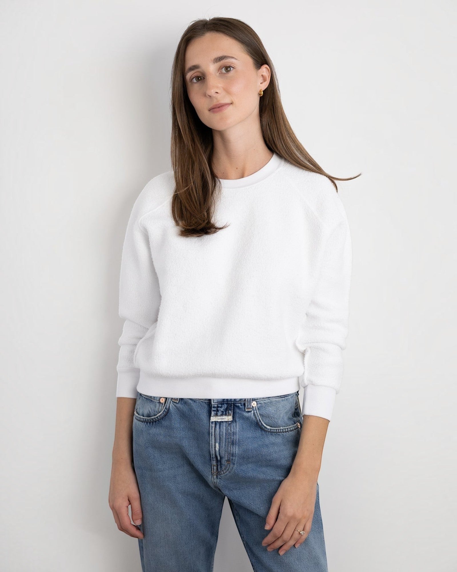 Model wearing a JONES + CO white Ziggy sweatshirt with a crew neck and cropped sleeves, paired with blue jeans.
